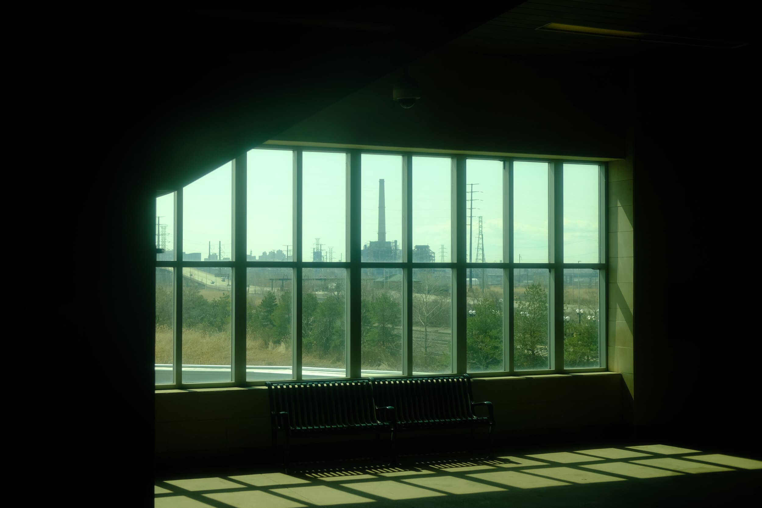 a dark, green tinged photo of a security camera above a bench inside of a train station.